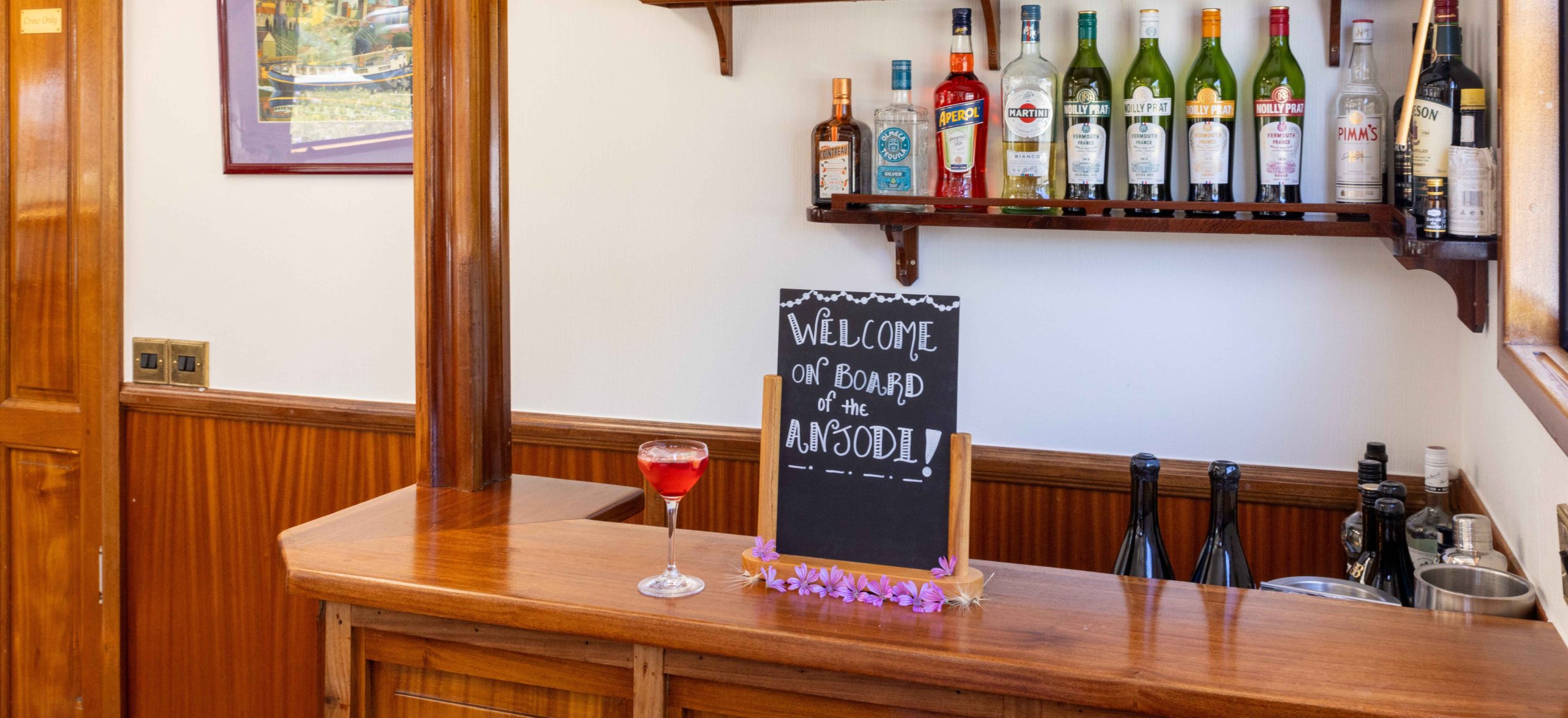 The saloon aboard hotel barge Anjodi, with wooden flooring, French dining furniture and a fully-stocked bar